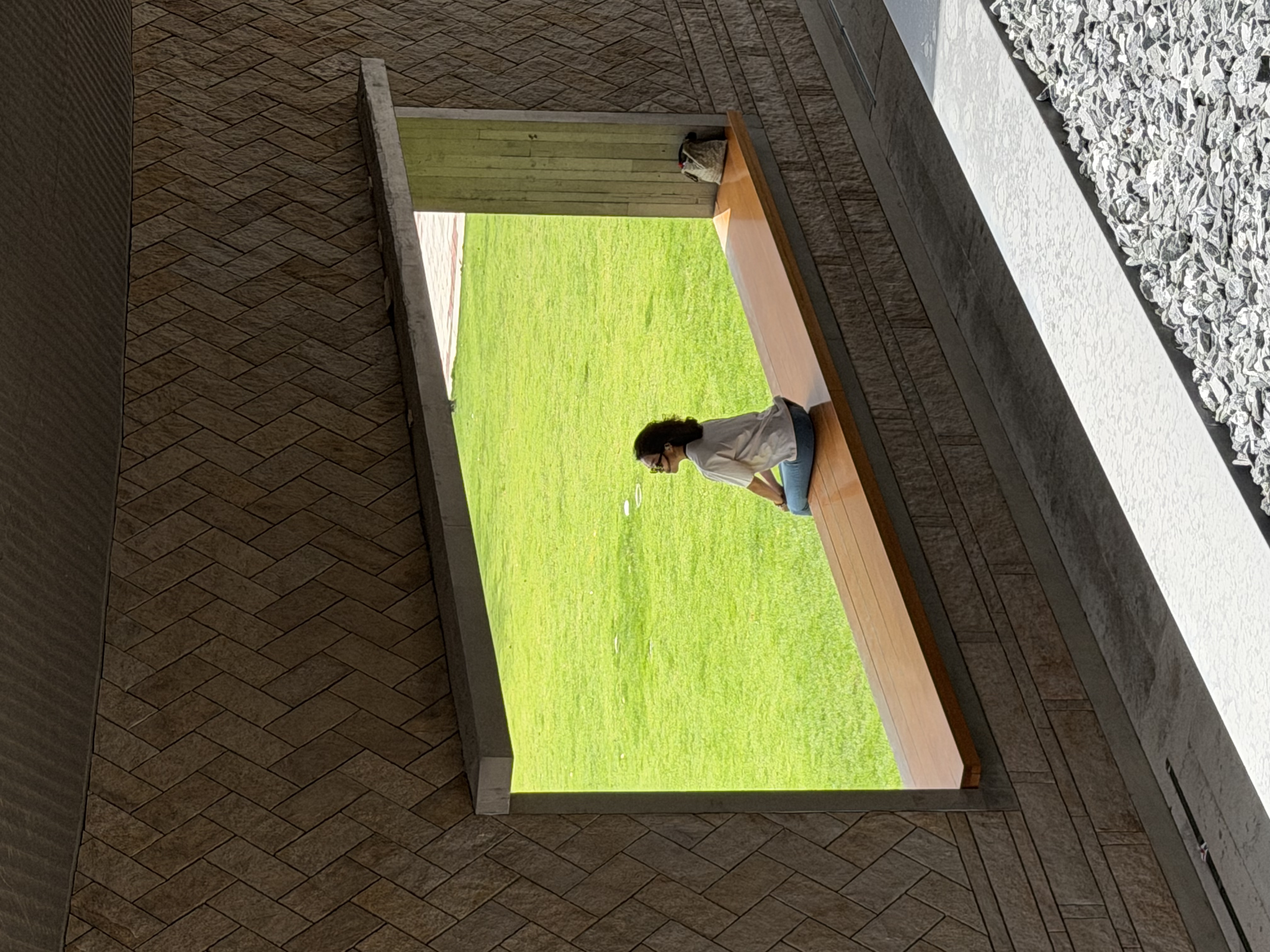 Malinna sitting at the edge of a window opening, looking toward a green lawn